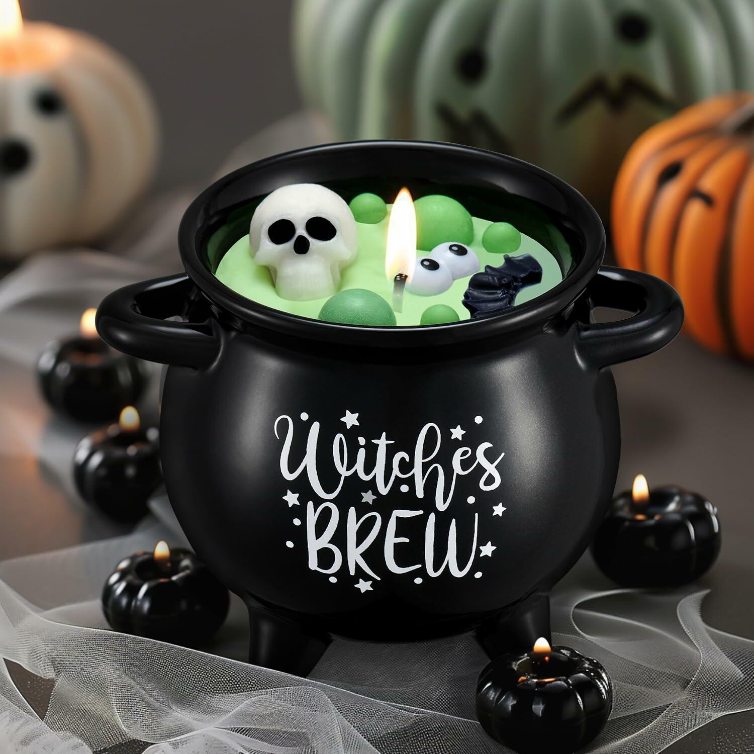 Halloween-themed candle in a black cauldron with floating skulls and green liquid, surrounded by pumpkins and small candles.