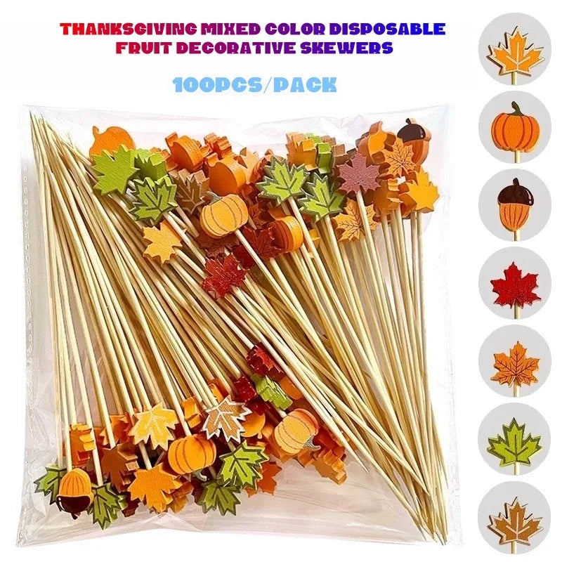 A 100-piece pack of Thanksgiving-themed disposable fruit skewers in a clear plastic bag, featuring autumn colors like orange, yellow, green, and red. The image includes a graphic on the right showing individual designs (pumpkin, acorn, maple leaf, etc.