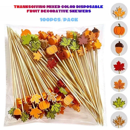 A 100-piece pack of Thanksgiving-themed disposable fruit skewers in a clear plastic bag, featuring autumn colors like orange, yellow, green, and red. The image includes a graphic on the right showing individual designs (pumpkin, acorn, maple leaf, etc.